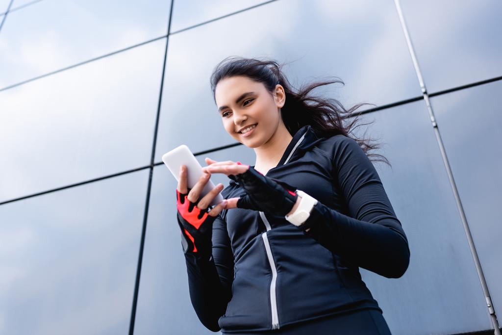 low angle view of happy sportswoman looking at smartphone  - Photo, Image