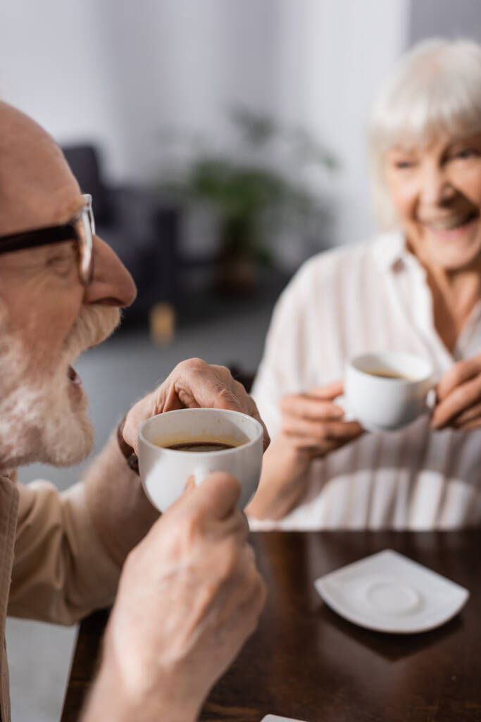 Selektiver Fokus positiver Senioren beim Kaffeetrinken in der Küche  - Foto, Bild