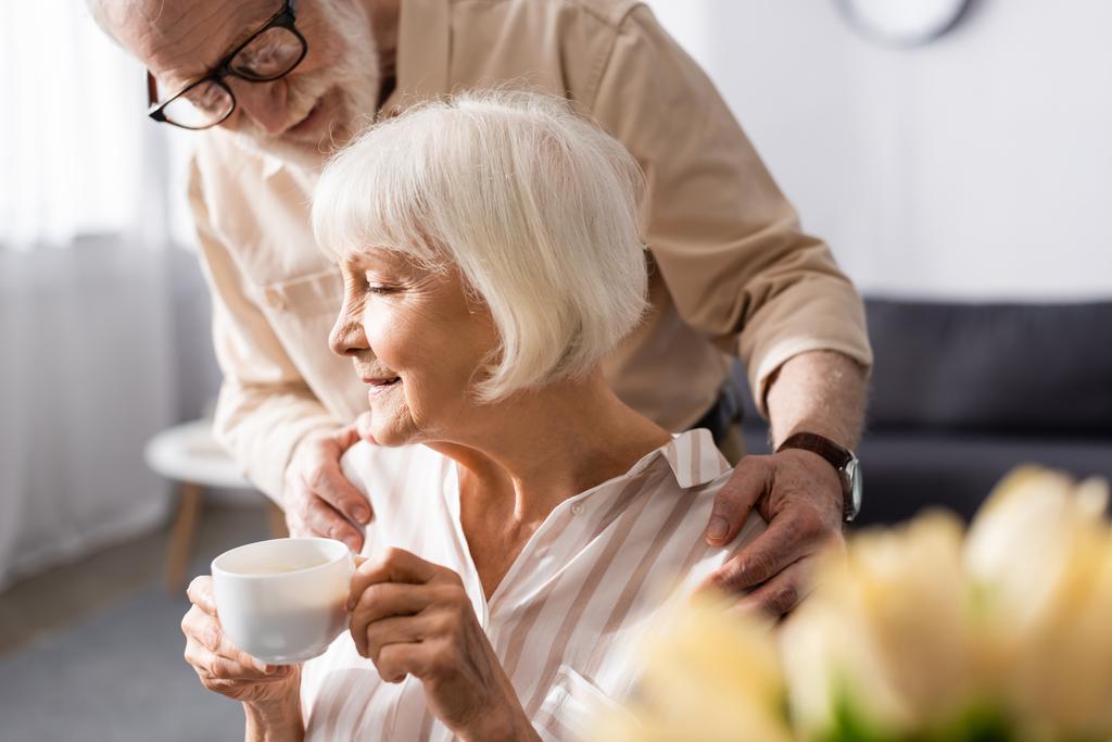 Selektywne skupienie człowieka senor przytulając żonę z filiżanką kawy podczas śniadania w domu - Zdjęcie, obraz
