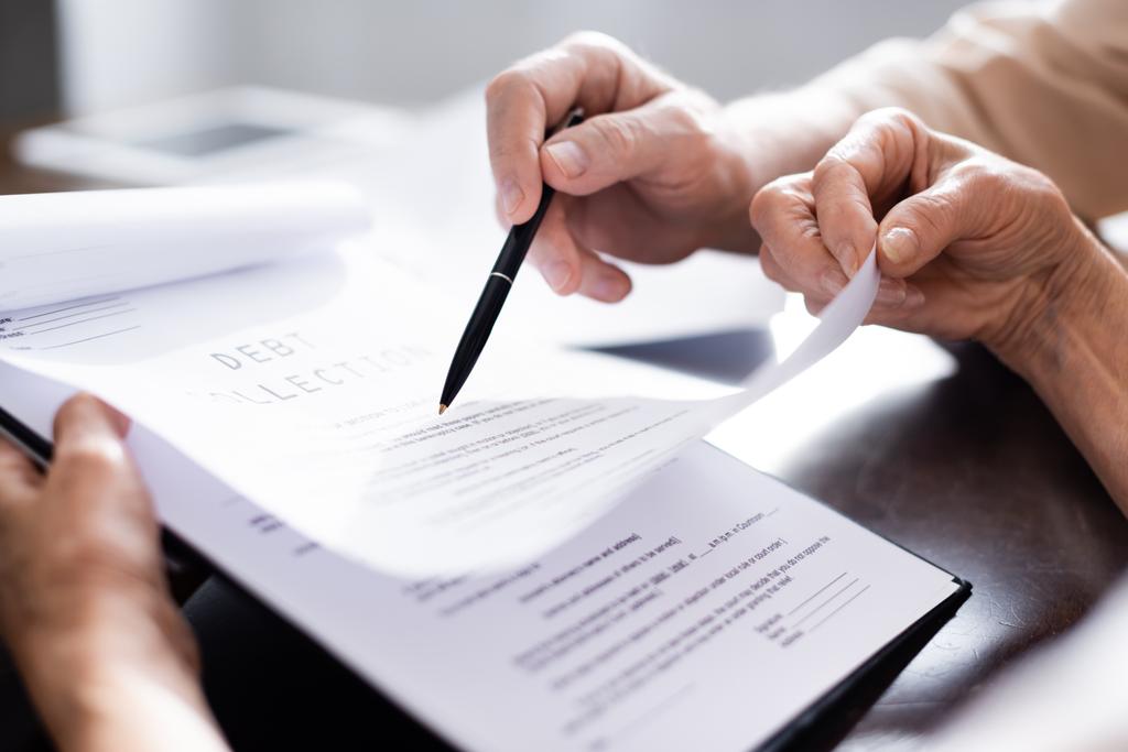Обрізаний вигляд літньої пари, що тримає ручку і документи з виписуванням боргу вдома
  - Фото, зображення