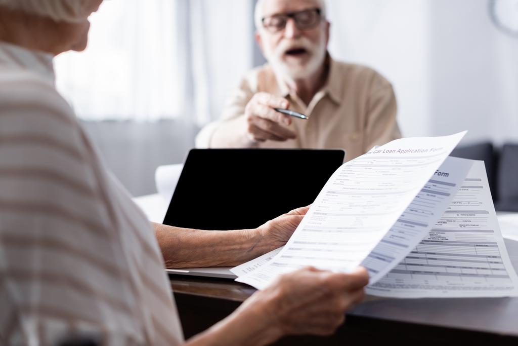 Válogatott fókusz idős férfi mutató feleség kezében papírok közelében laptop az asztalon   - Fotó, kép