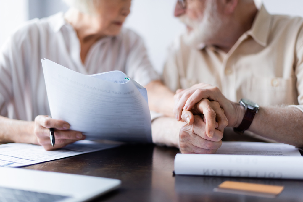 Widok pary seniorów trzymających się za ręce przy dokumentach, laptopie i karcie kredytowej na stole  - Zdjęcie, obraz