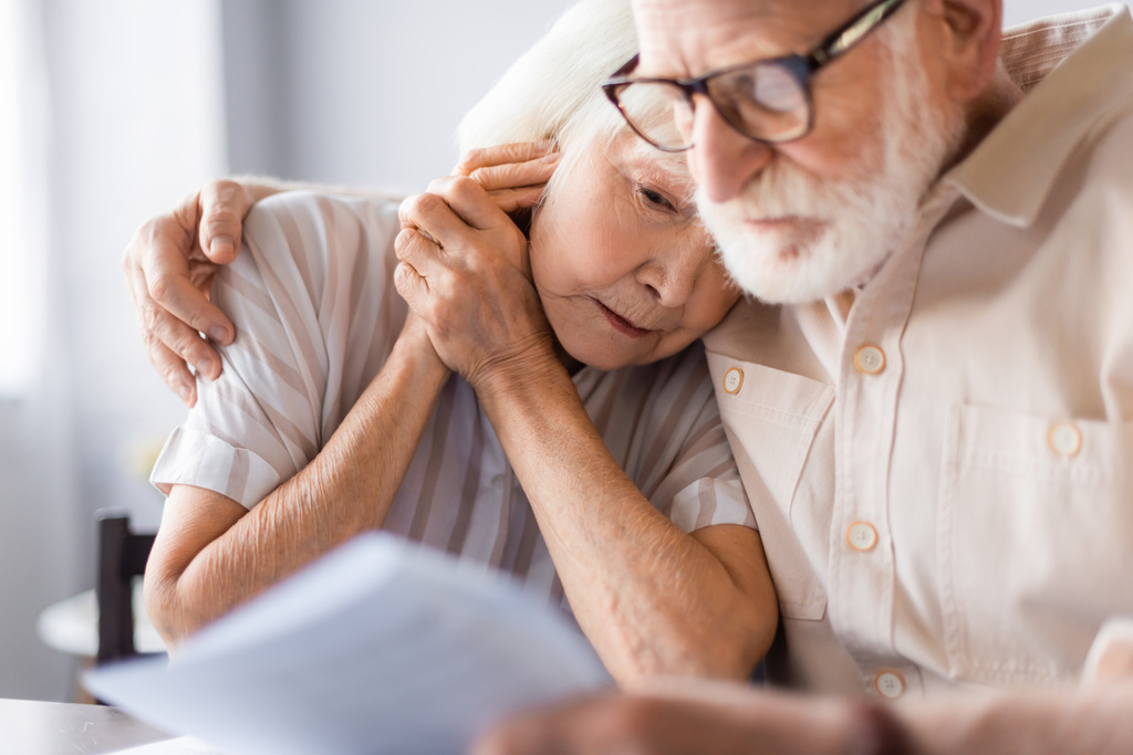 Selektivní zaměření staršího muže objímající rozrušenou ženu a držící papíry doma  - Fotografie, Obrázek