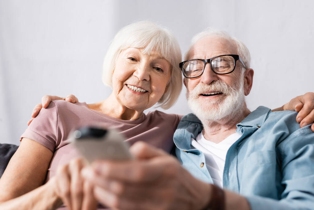 Selective focus of elderly couple smiling and holding remote controller of air conditioner at home  - Photo, Image