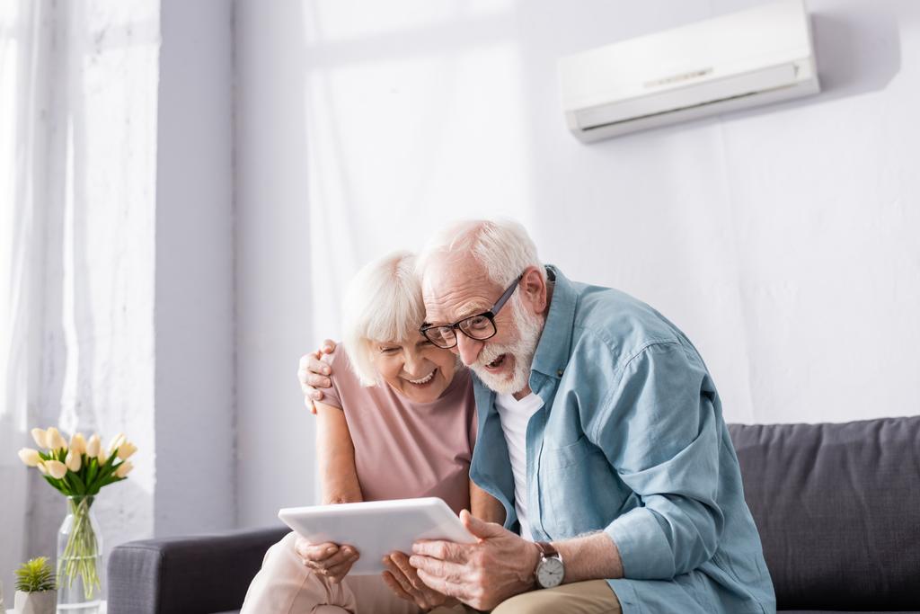 Positives Senioren-Coupé mit digitalem Tablet auf der heimischen Couch  - Foto, Bild