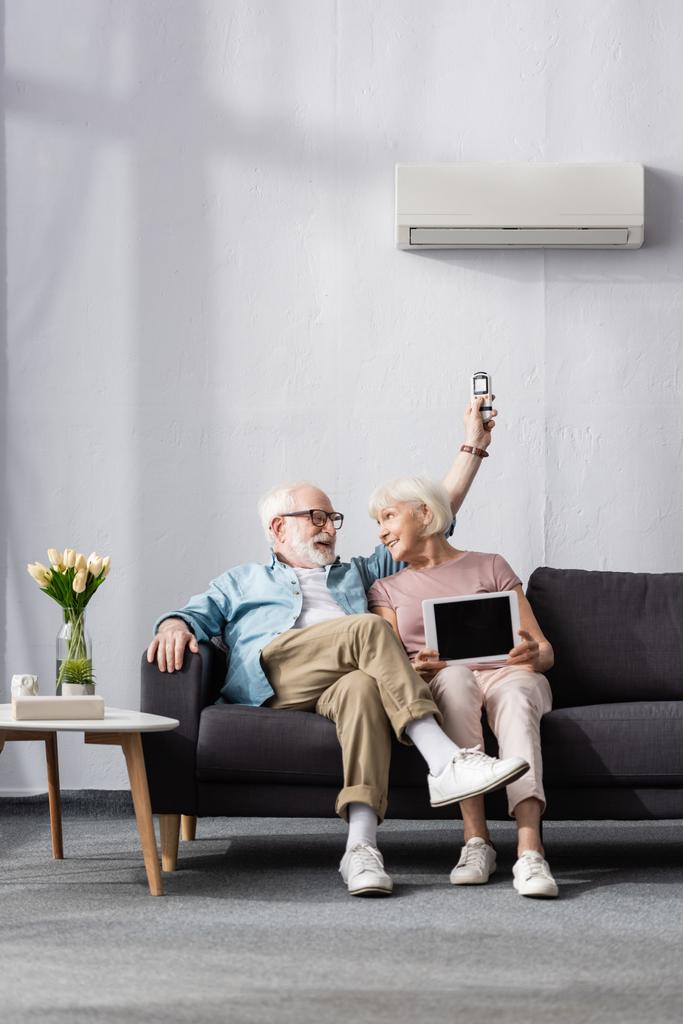 Hymyilevä vanhempi pari tilalla digitaalinen tabletti ja kaukosäädin ilmastointilaite kotona  - Valokuva, kuva