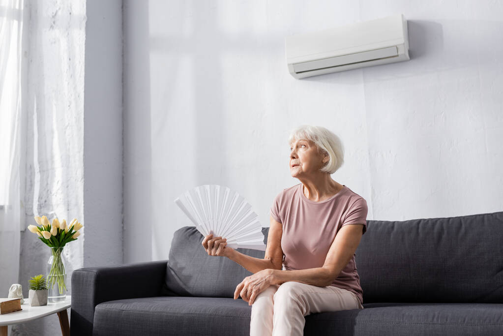 Літня жінка тримає вентилятор, страждаючи від спеки вдома
  - Фото, зображення