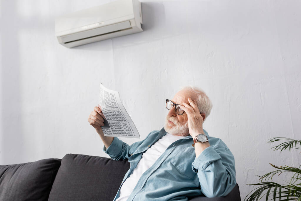Oudere man die thuis een krant op de bank houdt  - Foto, afbeelding