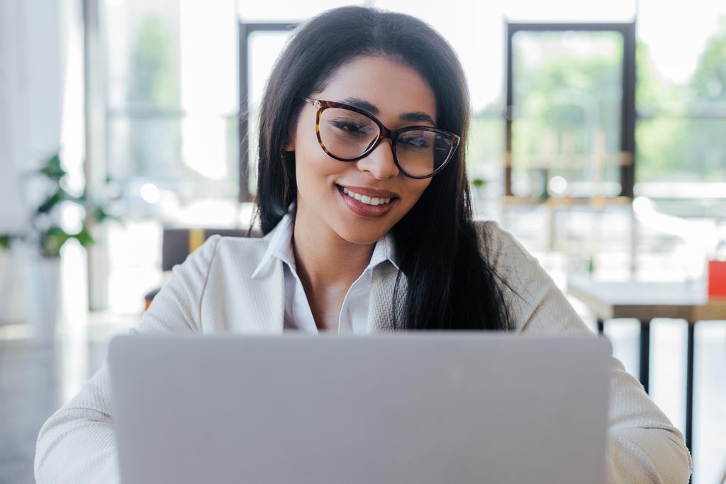 foco seletivo de empresária alegre em óculos usando laptop
  - Foto, Imagem