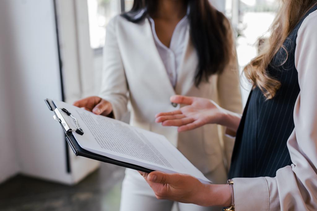 cropped view of businesswoman pointing with hand at clipboard near coworker in office  - Photo, Image