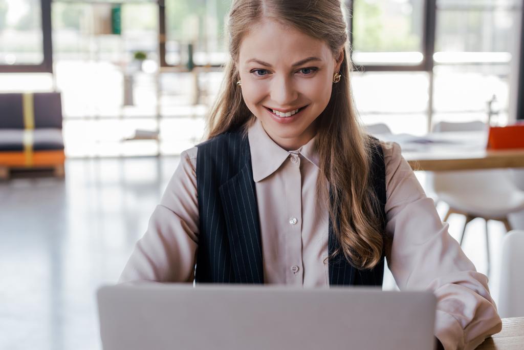 Selektiver Fokus glücklicher Geschäftsfrau mit Laptop im Büro  - Foto, Bild