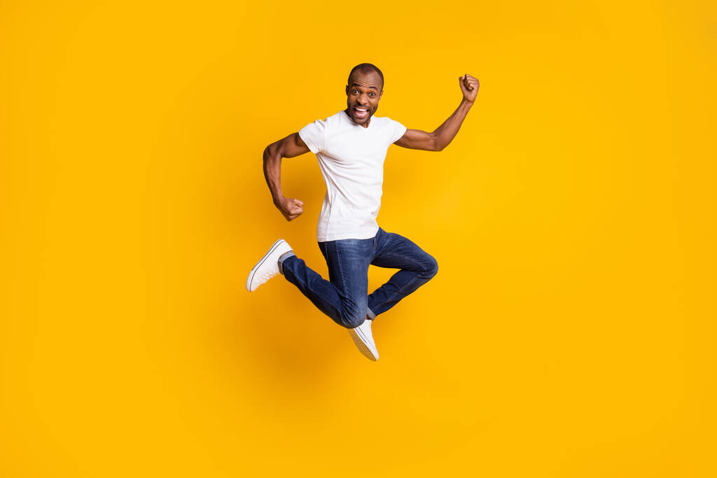 Full size foto van vrolijke blij afro-Amerikaanse man springen vieren korting lente tijd te winnen raise vuisten schreeuwen ja dragen spijkerbroek wit geïsoleerd over glans kleur achtergrond - Foto, afbeelding