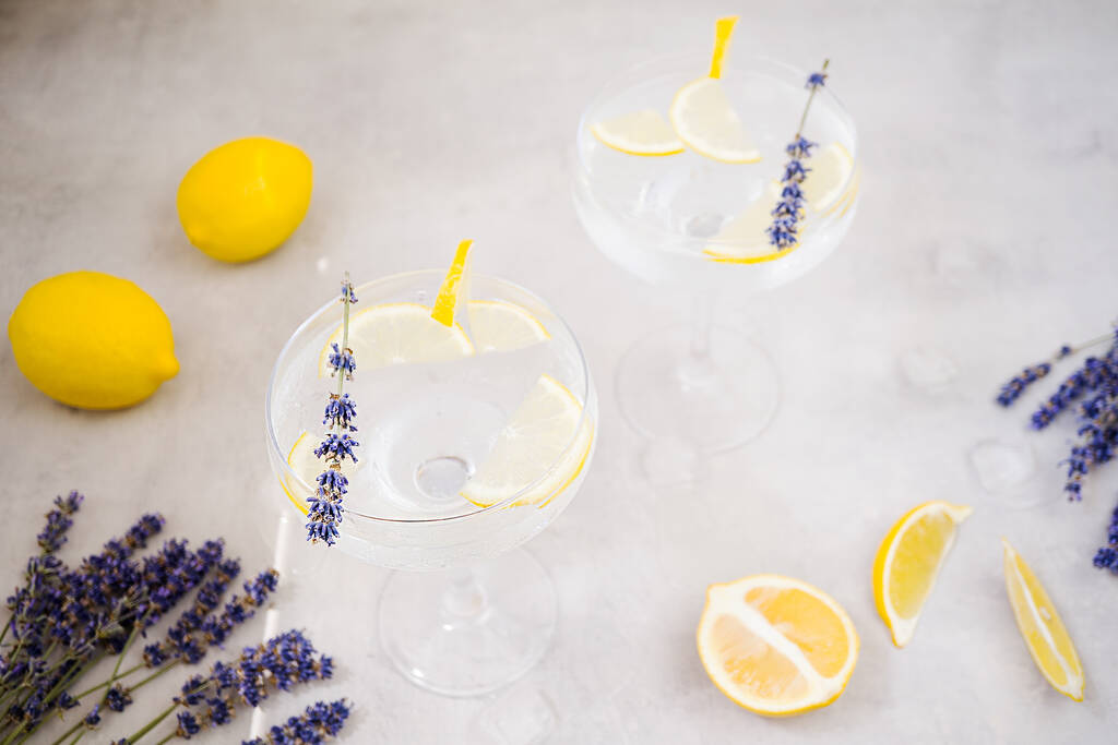 Refreshing infused water with lemon in beautiful glasses stands on a gray stone background. Glasses are decorated with a slice of lemon and lavender. Near are lemons. Detox morning drink, clean food. - Photo, Image