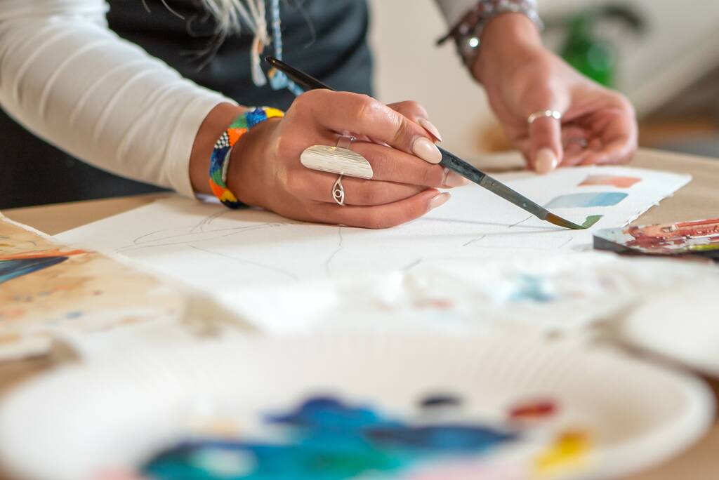 Eine Hochwinkelaufnahme einer Person, die mit Pinsel und Aquarellfarbe auf ein weißes Blatt Papier malt - Foto, Bild