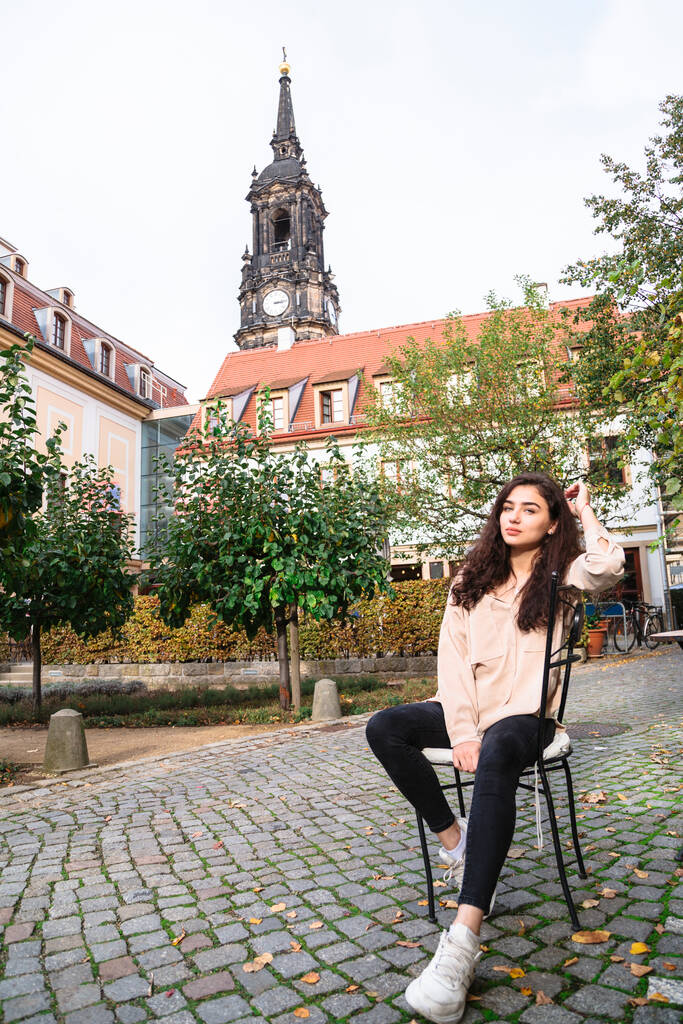 Brunetka dziewczyna siedzi na krześle w części starego miasta - Zdjęcie, obraz