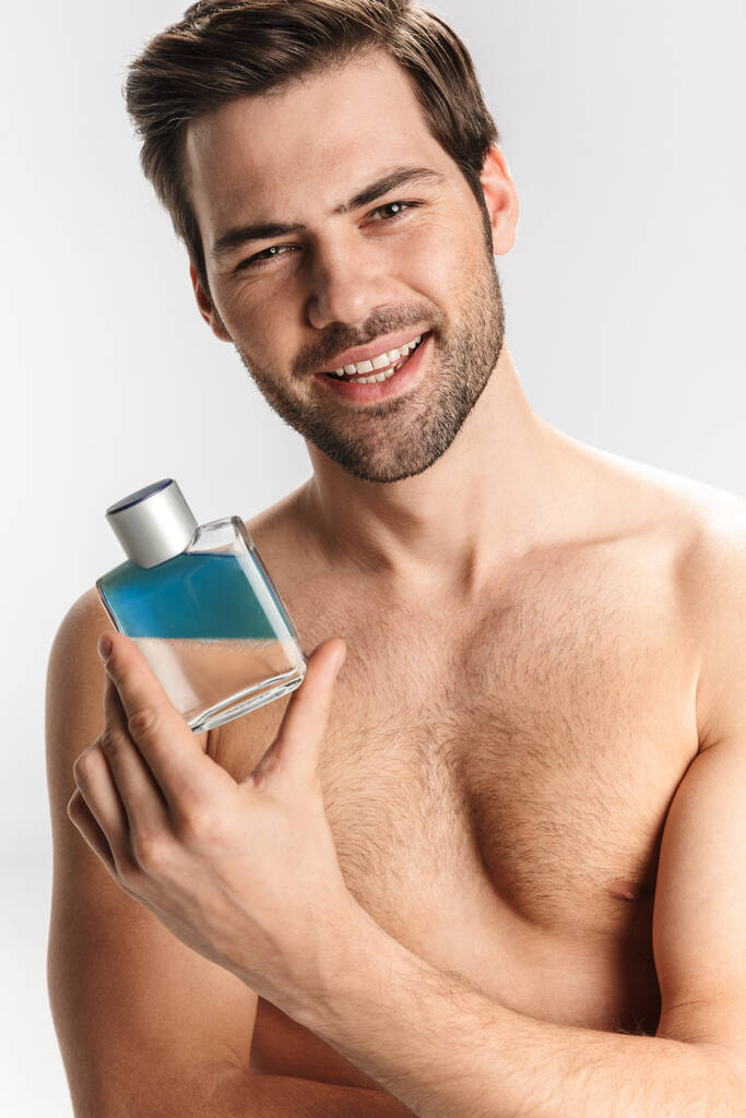 Photo of joyful half-naked man smiling and showing perfume isolated over white background - Photo, Image