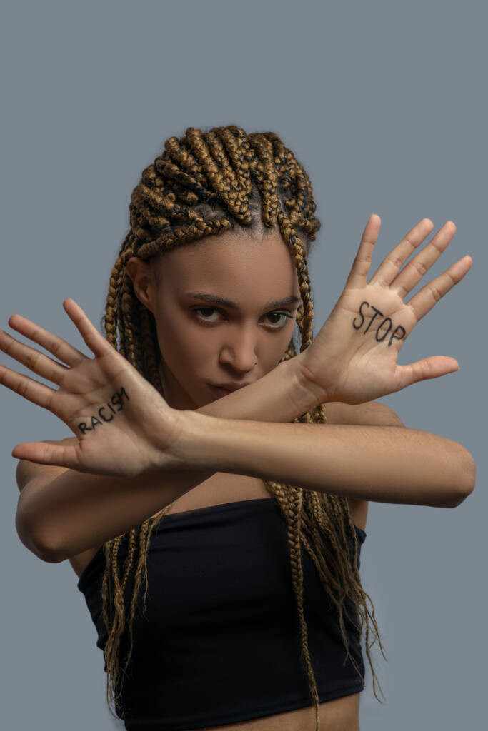Грустная молодая афроамериканка, скрещивающая руки, показывающая ладонь с расистскими надписями
 - Фото, изображение