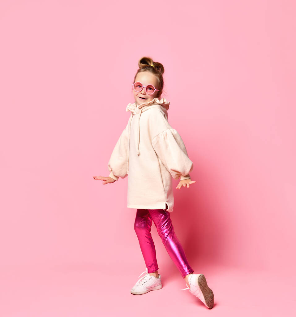alegre chica en elegante rosa gafas y leggings bailando posando sobre un fondo rosa claro. - Foto, imagen