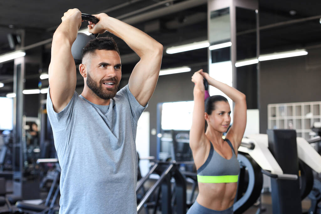 Подтянутая и мускулистая пара сосредоточилась на поднятии гантели во время занятий физкультурой в спортзале - Фото, изображение