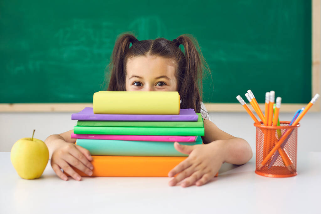 Смішна школярка тримає над головою книгу, сидячи на уроці в школі
. - Фото, зображення