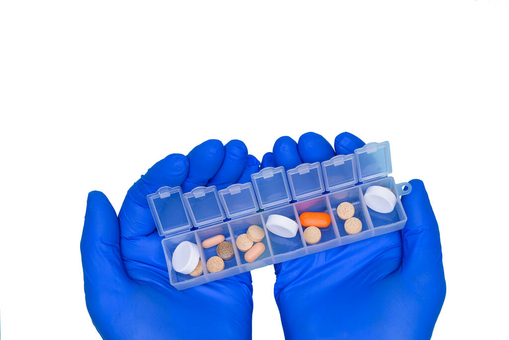 Руки лікаря в блакитних рукавичках, тримайте в руках коробку з ліками на кожен день, ізольовані на білому тлі. Медикаменти для лікування захворювання
. - Фото, зображення