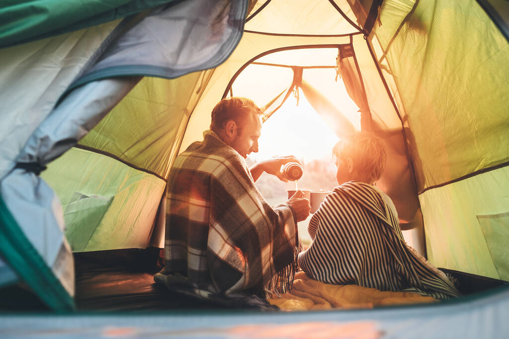 Отец и сын пьют горячий чай, сидя в палатке.
 - Фото, изображение