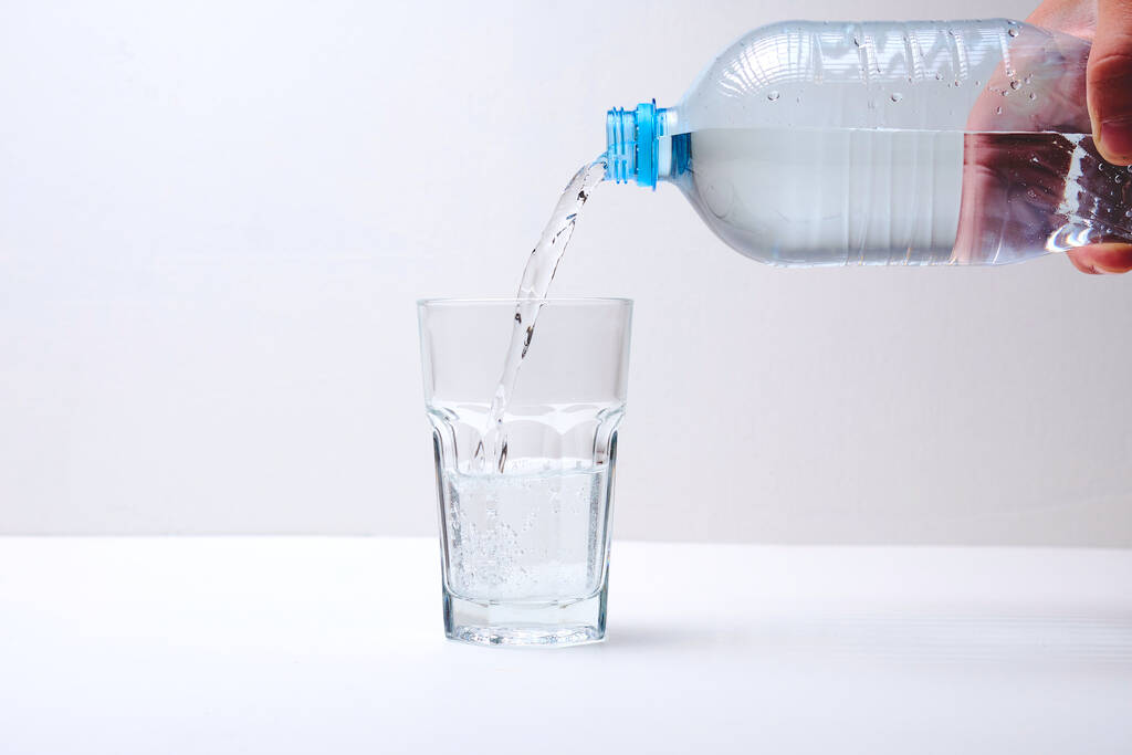 обрезанный снимок человека, наливающего воду из бутылки в стекло  - Фото, изображение