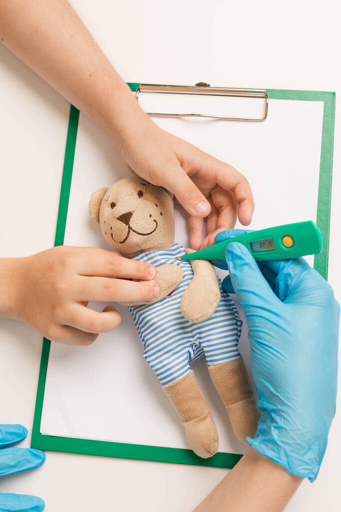 lekarz i dziecko trzymać termometr i zmierzyć temperaturę niedźwiedzia zabawki. - Zdjęcie, obraz