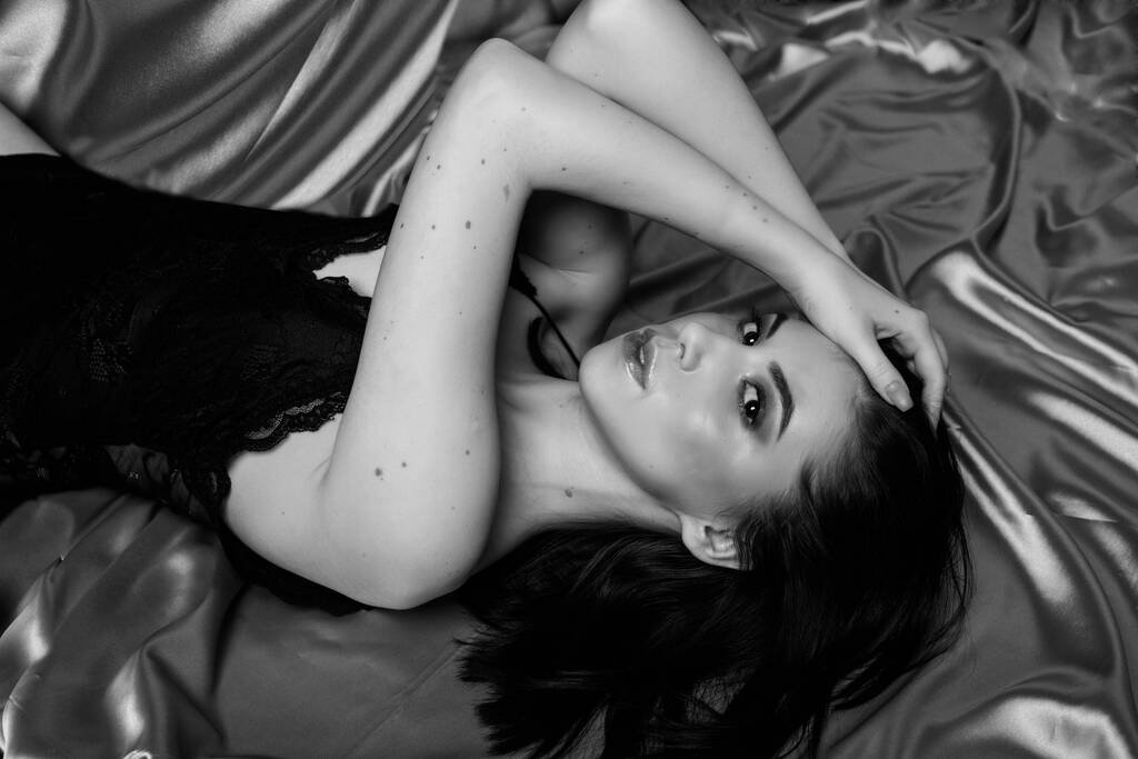 Fekete-fehér portré egy gyönyörű, szelíd lányról, sötét hajjal, szatén szöveten fekve. - Fotó, kép