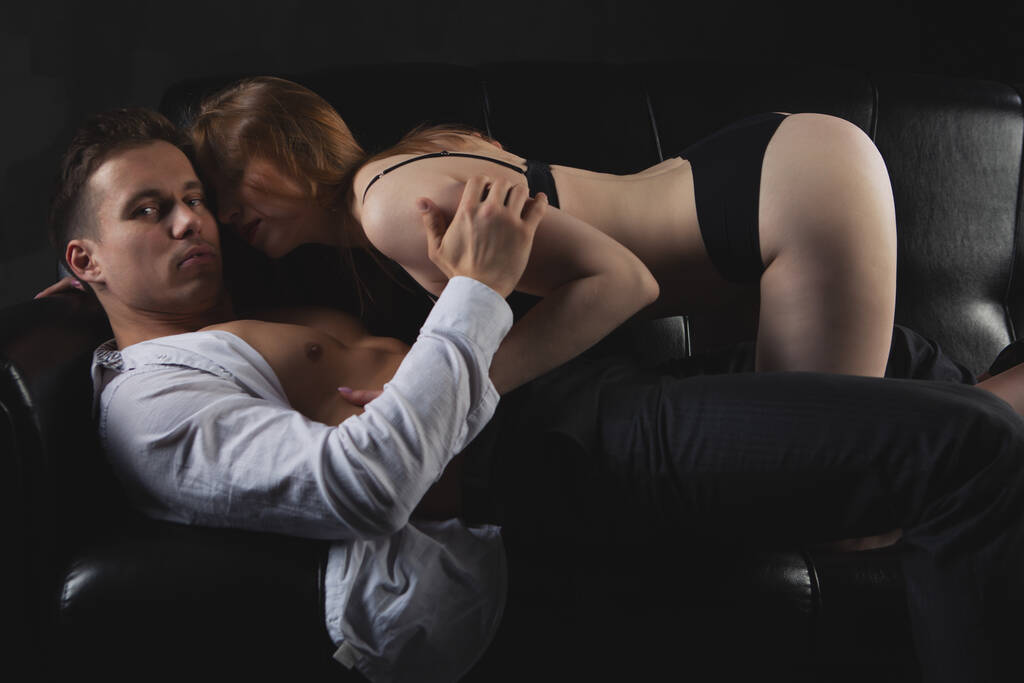Um jovem casal sexy despido, uma mulher sensual com um corpo sexy em roupa interior erótica preta beija um homem bombeado gradualmente despir-se dele
 - Foto, Imagem