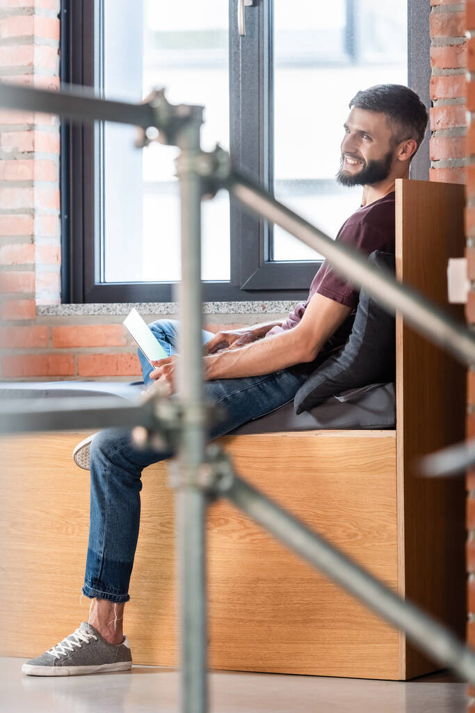 szelektív fókusz boldog üzletember ül ablak pad és a laptop  - Fotó, kép