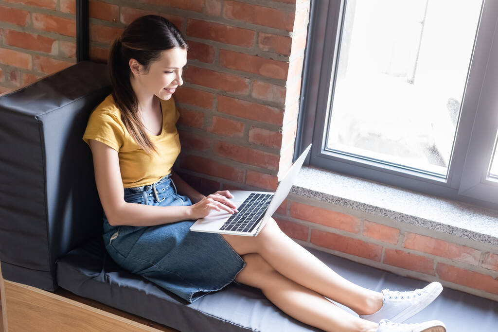 gelukkig zakenvrouw zitten op het raam bank en met behulp van laptop in het kantoor  - Foto, afbeelding