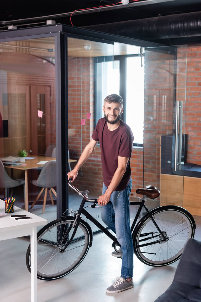 cheerful businessman standing with bicycle in modern office  - Photo, Image