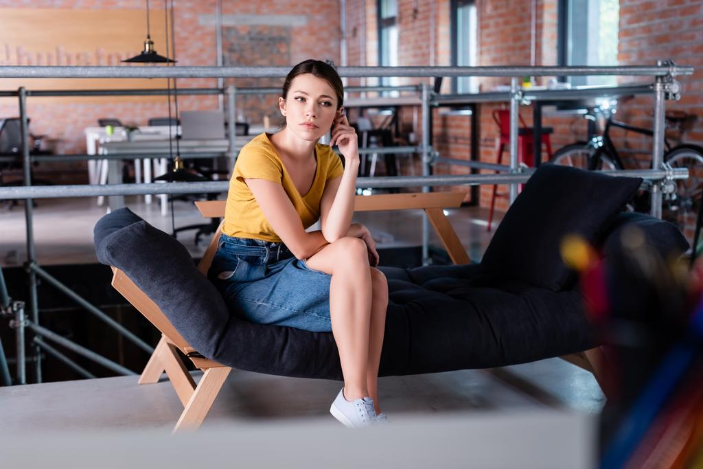 επιλεκτική εστίαση της ελκυστική επιχειρηματίας κάθεται σε καναπέ στο σύγχρονο γραφείο - Φωτογραφία, εικόνα