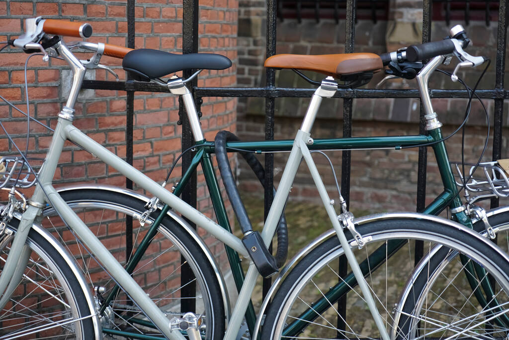 δύο κλασικά ποδήλατα που στέκονται σε κλειδαριά σε μαύρο μεταλλικό φράχτη. Ευρωπαϊκός δρόμος. μοντέρνο ποδήλατο. Haag, Κάτω Χώρες. - Φωτογραφία, εικόνα