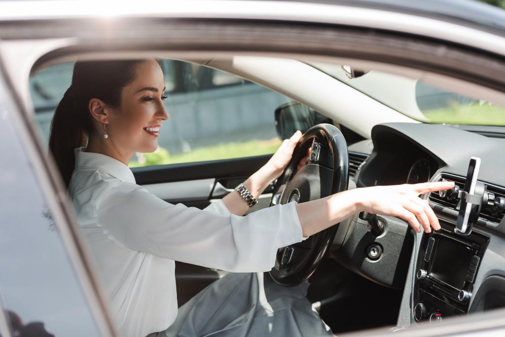 Boční pohled na usmívající se podnikatelka pomocí smartphone při jízdě auto  - Fotografie, Obrázek