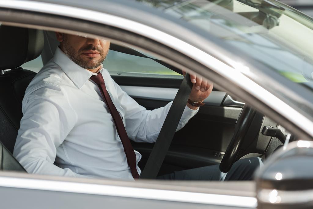 Селективный фокус бизнесмена, держащего ремень безопасности в автомобиле
  - Фото, изображение