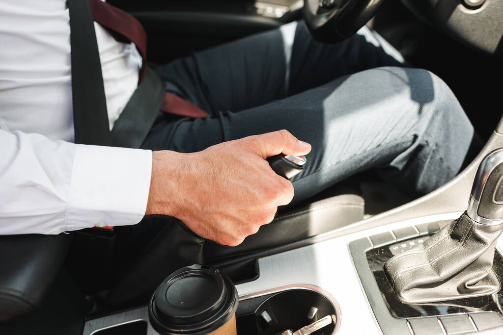 Обрезанный вид бизнесмена в формальной одежде вождения автомобиля рядом с кофе, чтобы пойти в держатель кубка
 - Фото, изображение