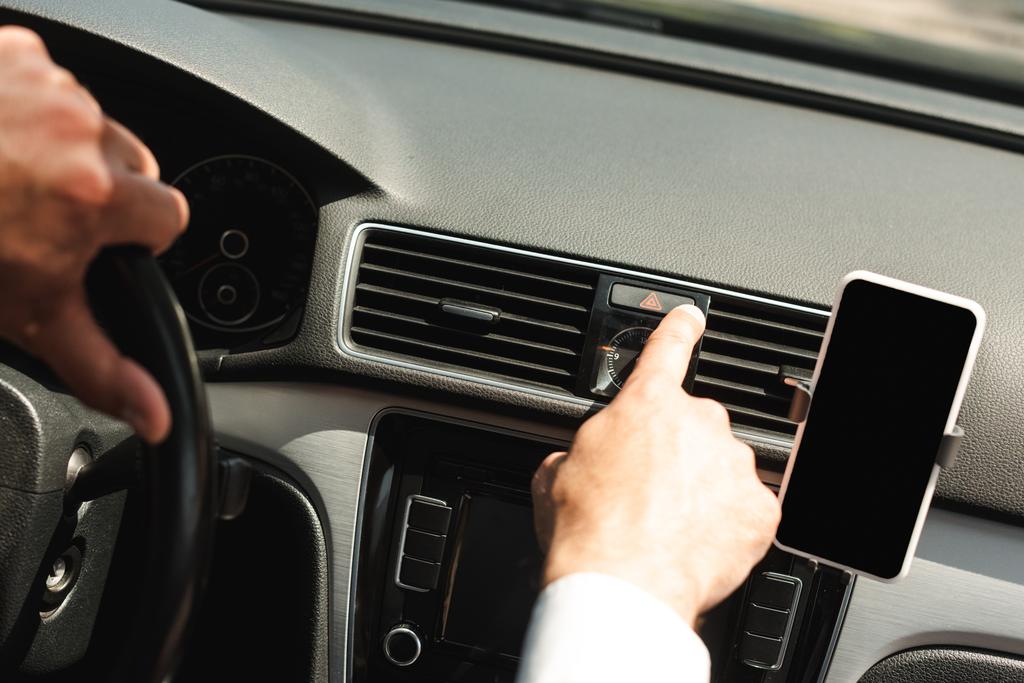 Vista recortada del hombre que enciende la señal de advertencia cerca del teléfono inteligente mientras conduce el coche
 - Foto, imagen