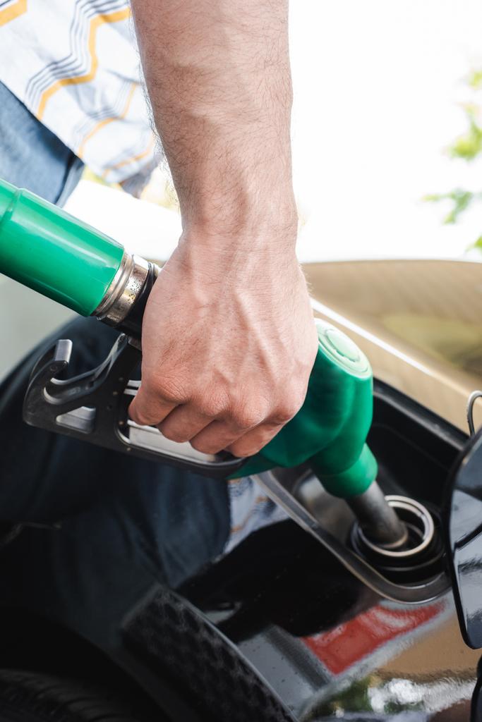 Cropped view of man holding fueling nozzle near open gas tank cover outdoors - Photo, Image
