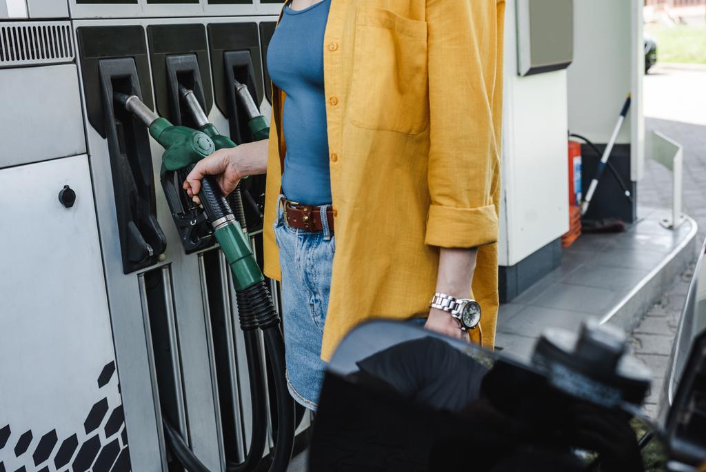 Cropped view of woman taking fueling nozzle near auto on gas station on urban street  - Photo, Image