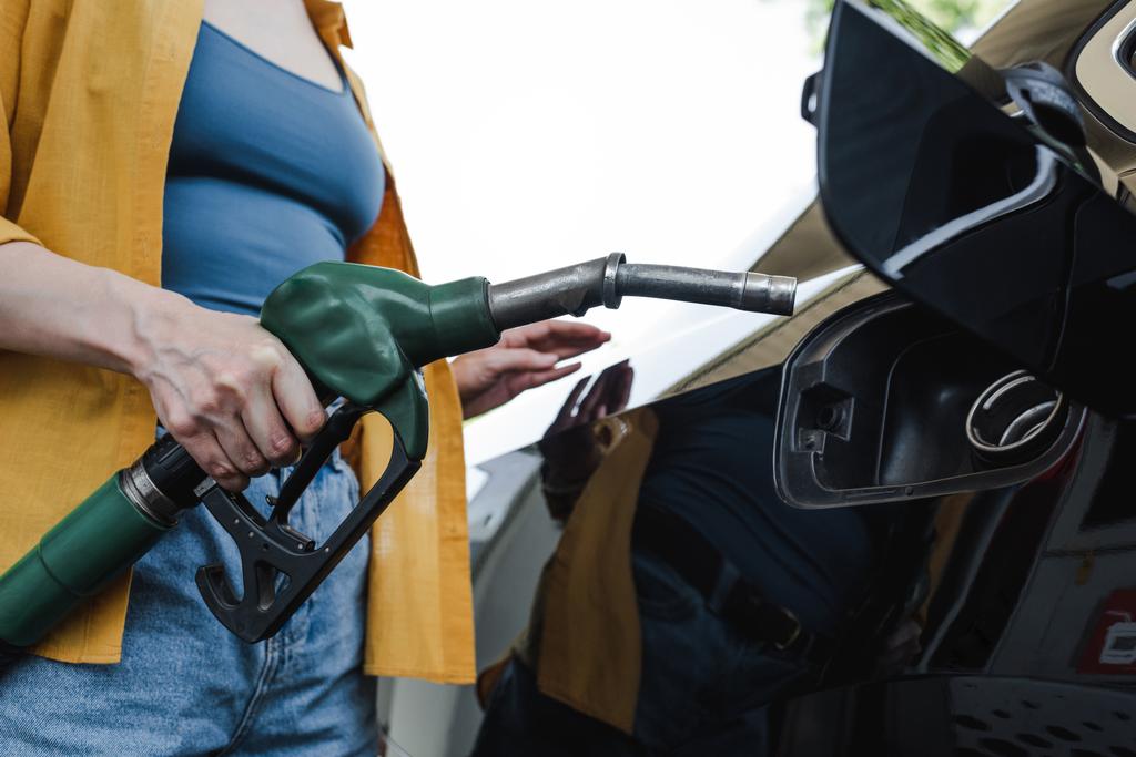 Καλλιεργημένη άποψη της γυναίκας που κρατά ακροφύσιο τροφοδοσίας κοντά στο auto στο βενζινάδικο  - Φωτογραφία, εικόνα