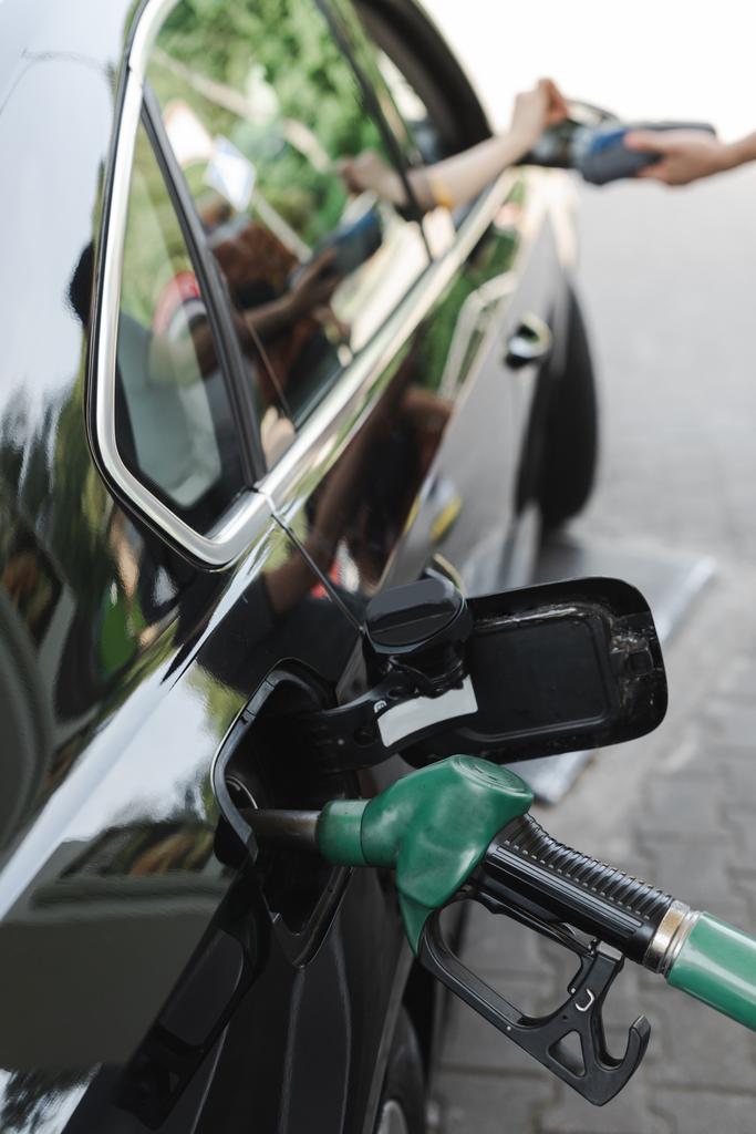 Selectieve focus van tanken mondstuk in gastank van auto en vrouw betalen met credit card op tankstation  - Foto, afbeelding