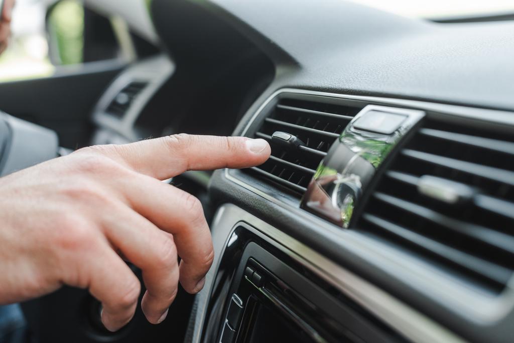Gewassen beeld van de mens het aanpassen van airconditioner op dashboard in auto  - Foto, afbeelding