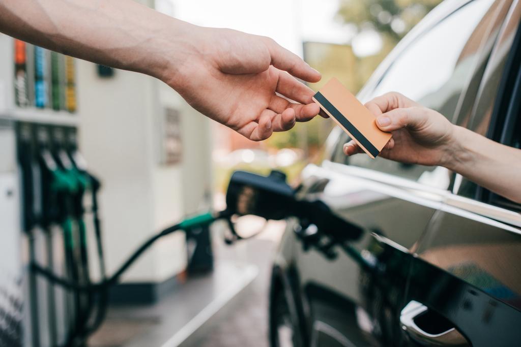 Widok kobiety podającej kartę kredytową pracownikowi stacji benzynowej podczas tankowania samochodu   - Zdjęcie, obraz