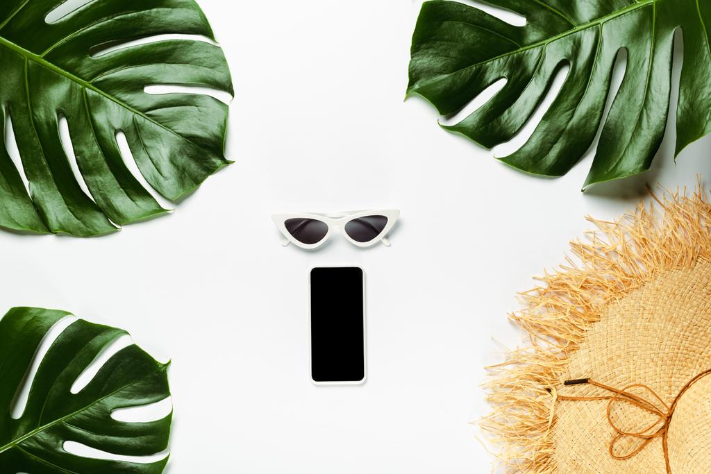 πάνω όψη πράσινων φύλλων φοίνικα, ψάθινο καπέλο, γυαλιά ηλίου και σημειωματάριο με smartphone σε λευκό φόντο - Φωτογραφία, εικόνα