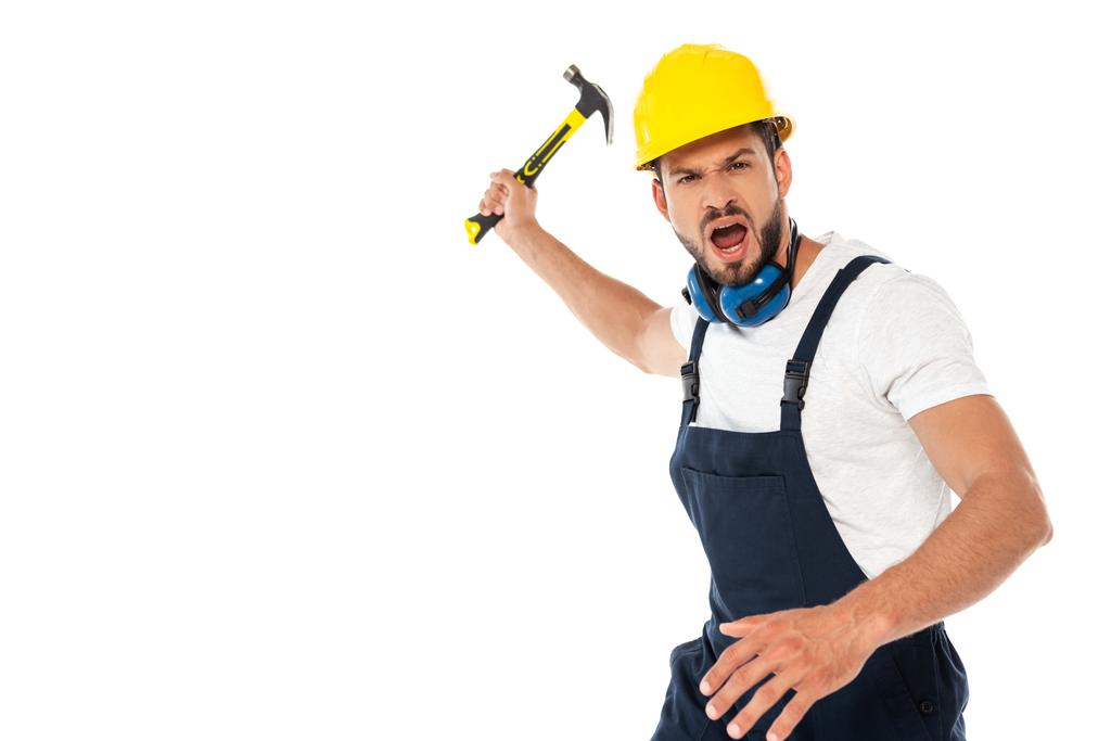 Wütender Arbeiter in Uniform und Harthut schreit, während er Hammer isoliert auf Weiß hält - Foto, Bild