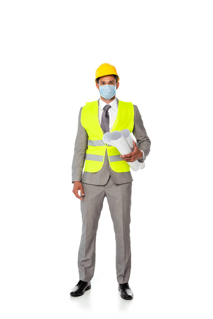 Ingegnere in tuta, casco di sicurezza e maschera medica con cianografie su sfondo bianco - Foto, immagini