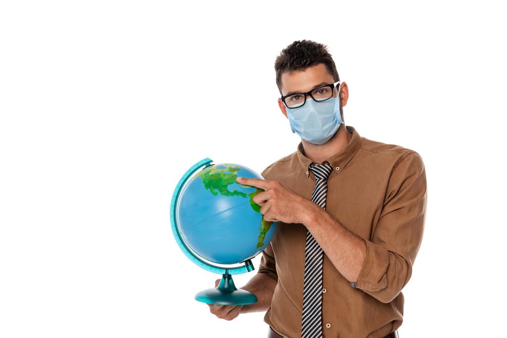 Profesor en máscara médica apuntando con el dedo al globo y mirando a la cámara aislada en blanco
 - Foto, Imagen