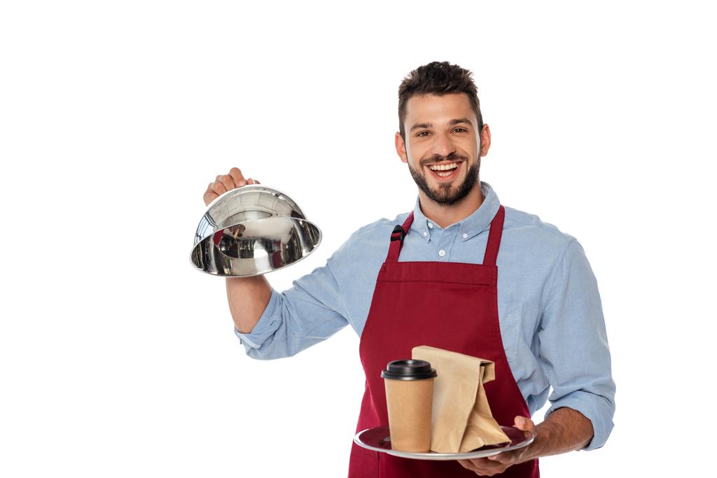 Χαρούμενος σερβιτόρος κρατώντας χάρτινο κύπελλο και τσάντα σε δίσκο και κάλυμμα πιάτων που απομονώνονται σε λευκό - Φωτογραφία, εικόνα